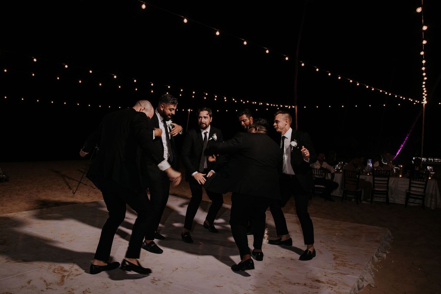 Wedding guests dance in a line on an illuminated dance floor under string lights.