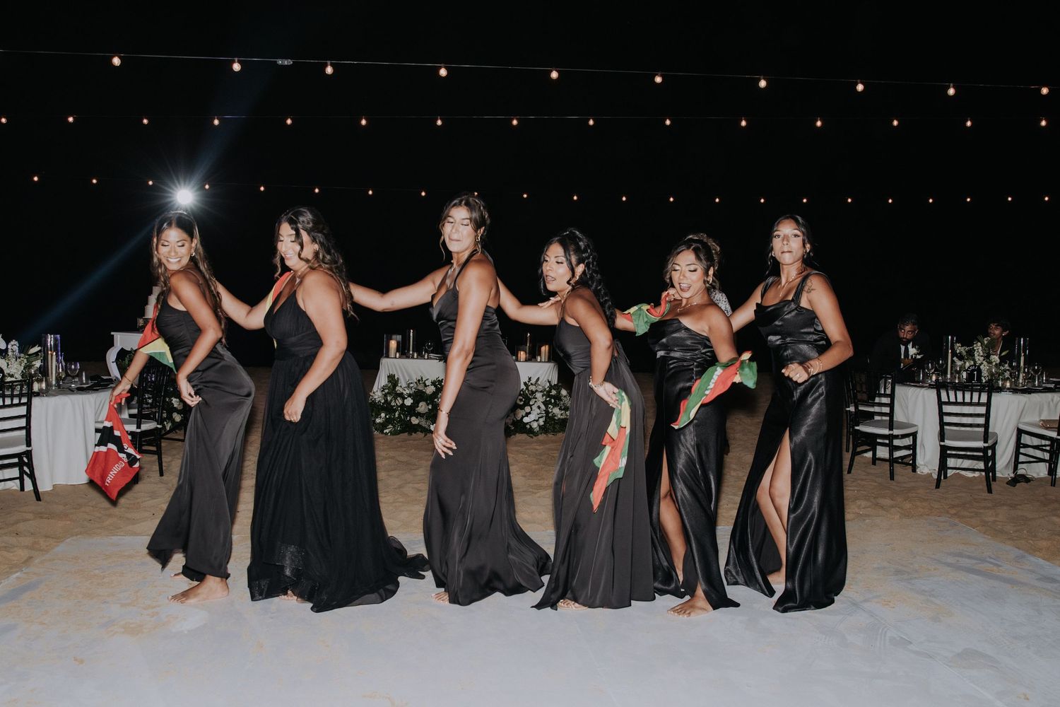 Group in formal black attire performs choreographed dance moves at a nighttime celebration.