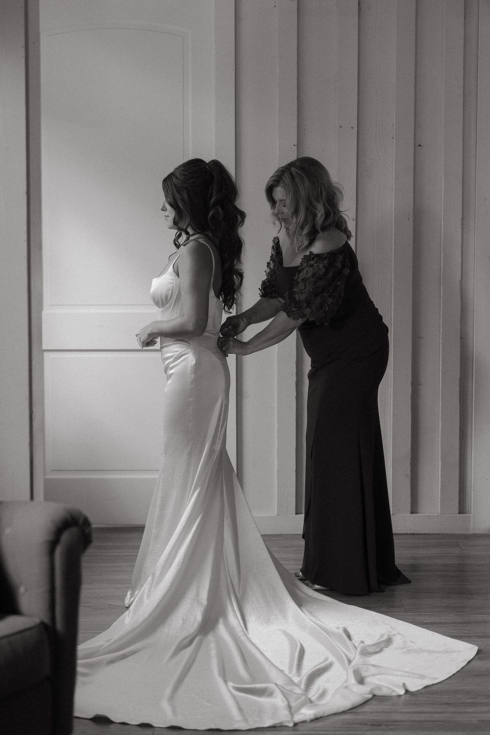 Candid black and white photo of a wedding dress being fitted and adjusted in a bright studio space.