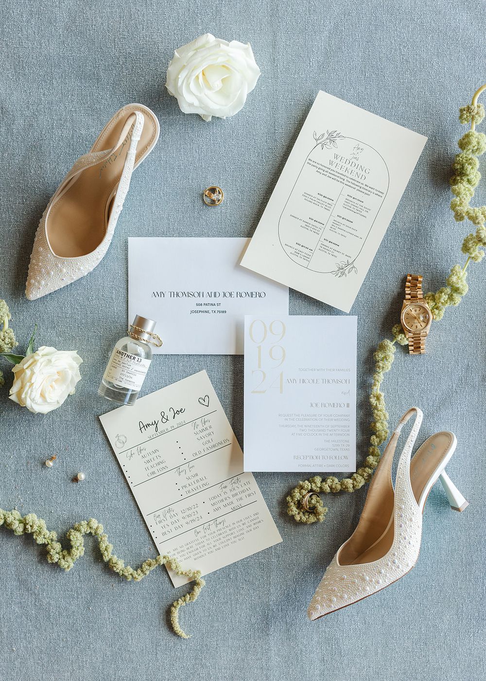 Elegant wedding stationery and nude heels arranged with white roses on grey linen background for flat lay styling.
