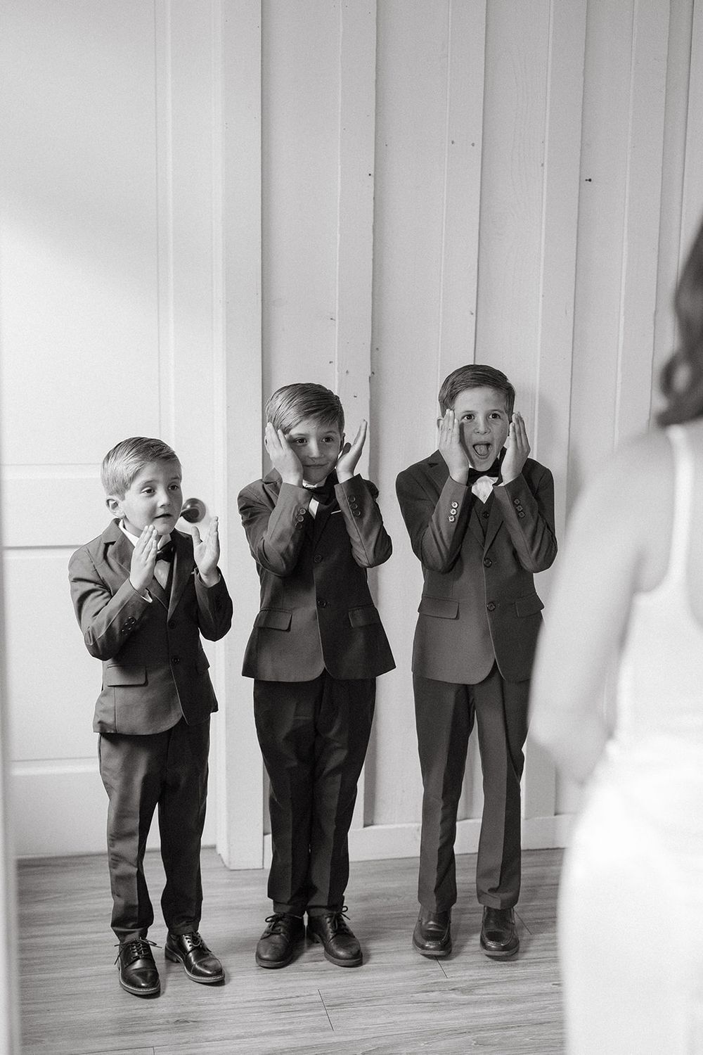 A black and white photo of three young children in suits standing against a white wall while covering their faces.