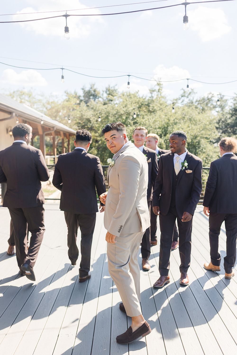 Groomsmen lined up on a wooden deck under string lights at an outdoor wedding venue.