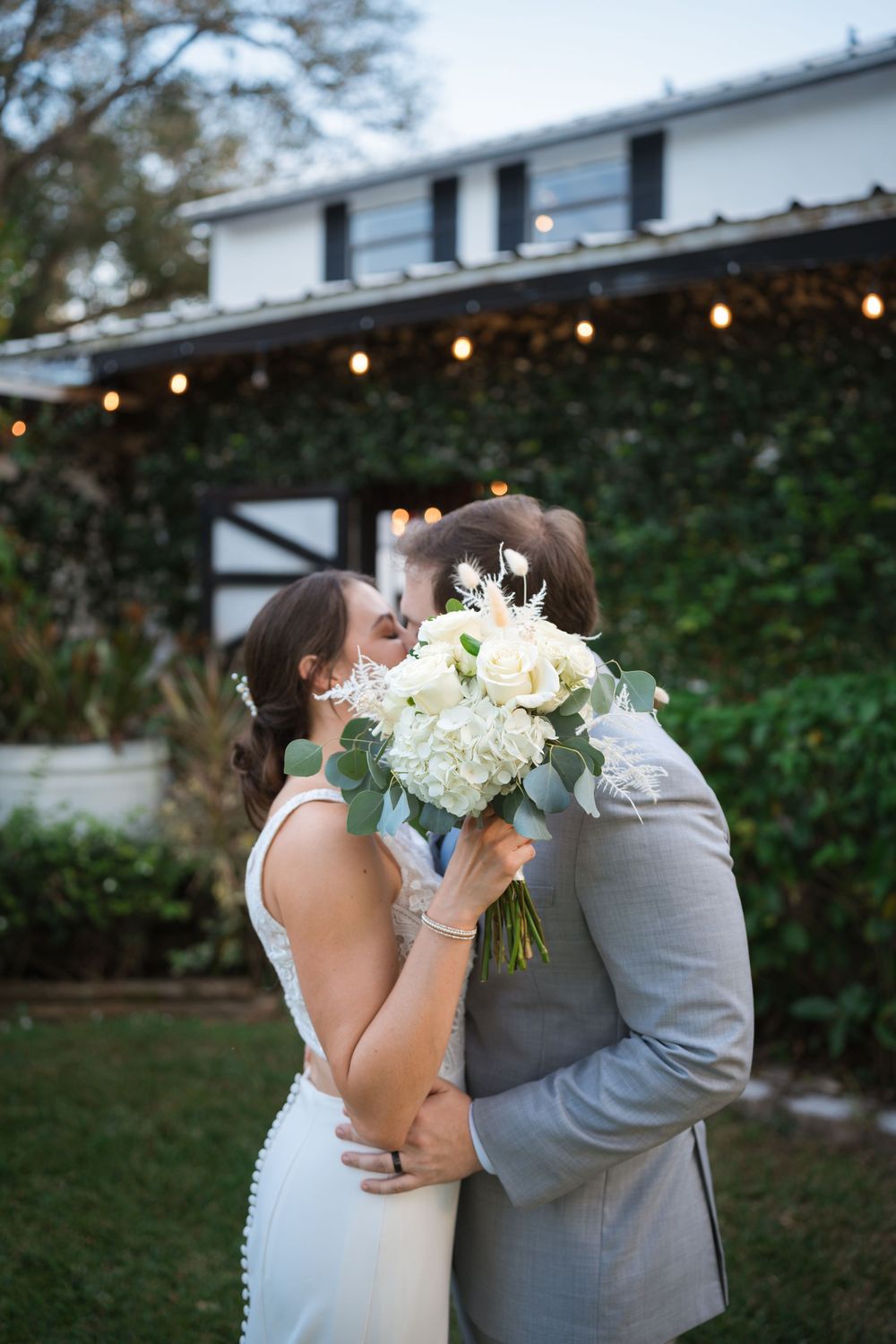 A series of candid wedding photos showing the newlyweds embracing while holding a white floral bouquet in an outdoor garden.