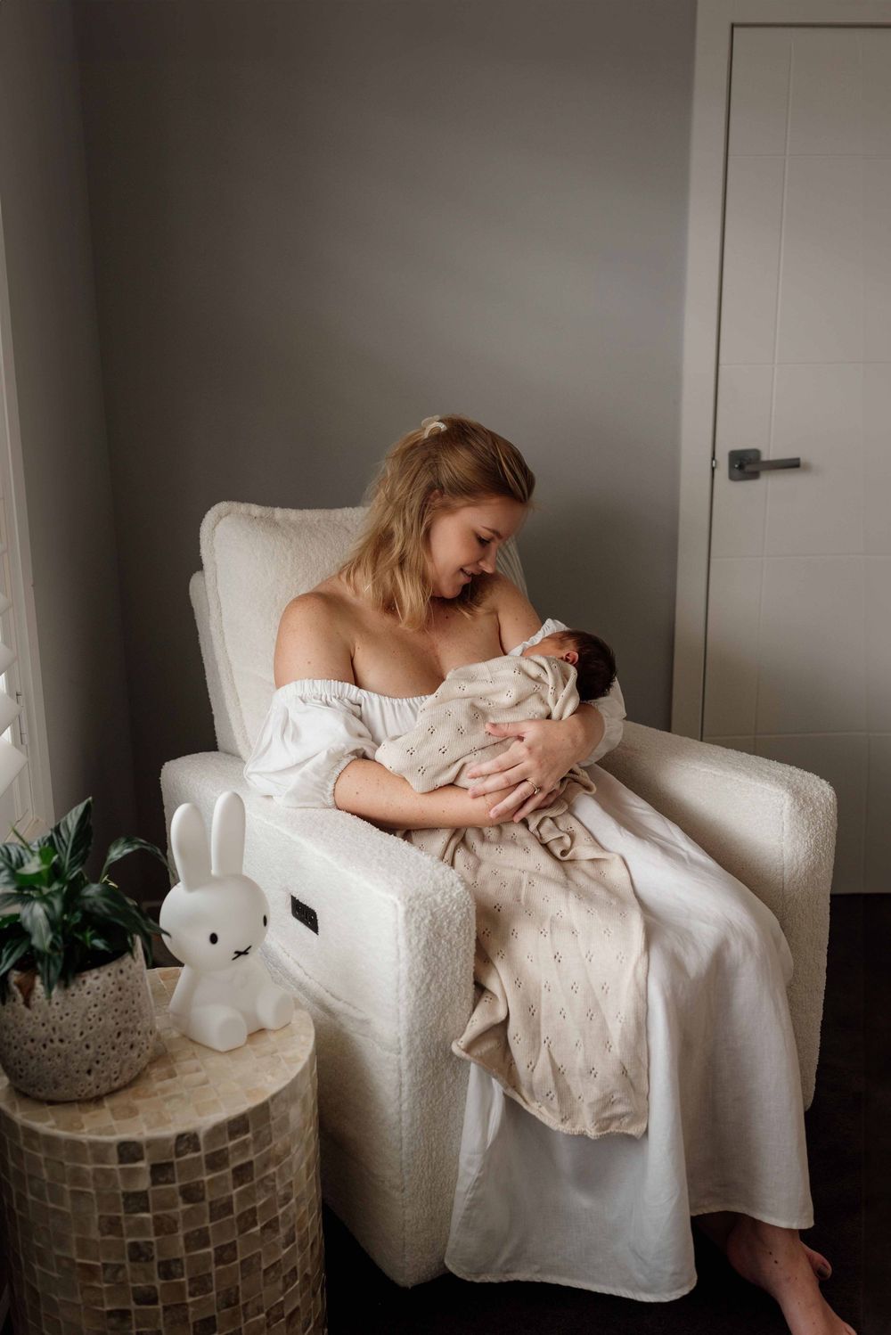 Mother sitting in nursing chair with newborn during in-home photoshoot, Sydney.