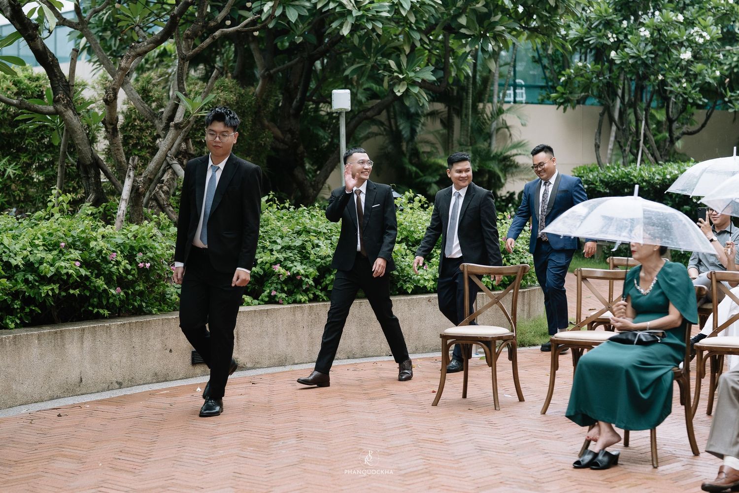 Wedding guests and groomsmen walking through an outdoor garden venue on a wedding day.