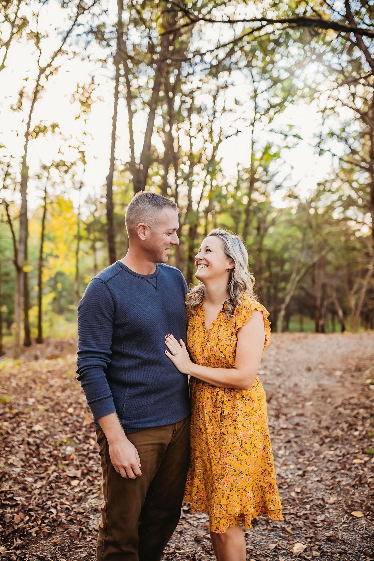 A couple shares a joyful moment together on a leaf-covered path in an autumn forest setting.