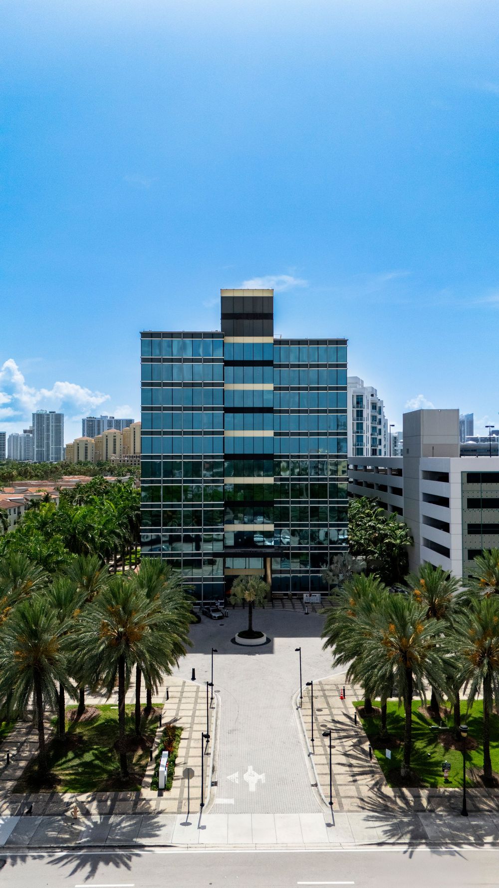 Modern office complex with palm tree lined plaza and glass facade buildings.