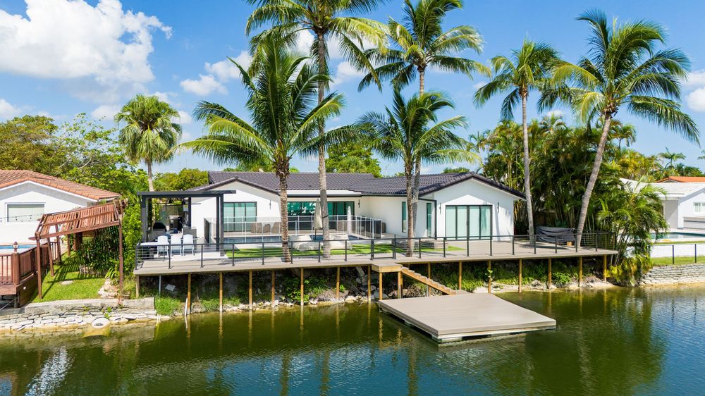 Drone panorama of palm-lined waterfront properties with private docks along Miami canal.
