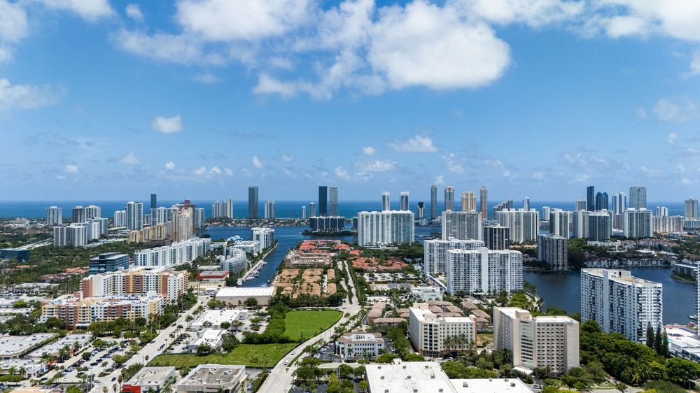 Aerial panoramic view of Miami Beach coastline showing luxury condominiums and white sand beaches against blue sky.