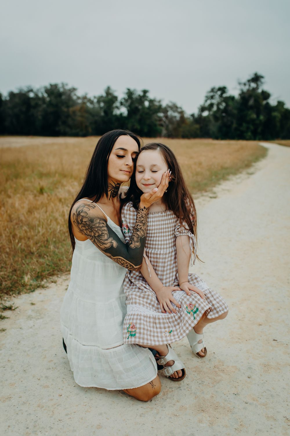 Two people share a tender moment on a dirt path surrounded by golden fields and trees.