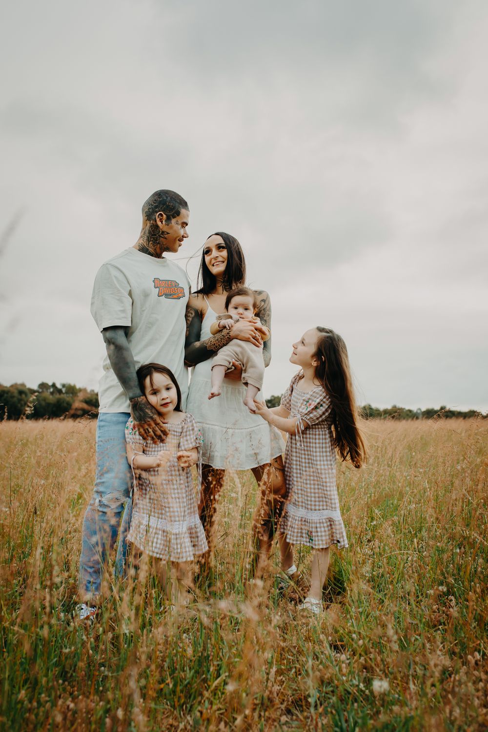 A family wearing coordinated outfits stands together in a golden wildflower meadow on an overcast day.