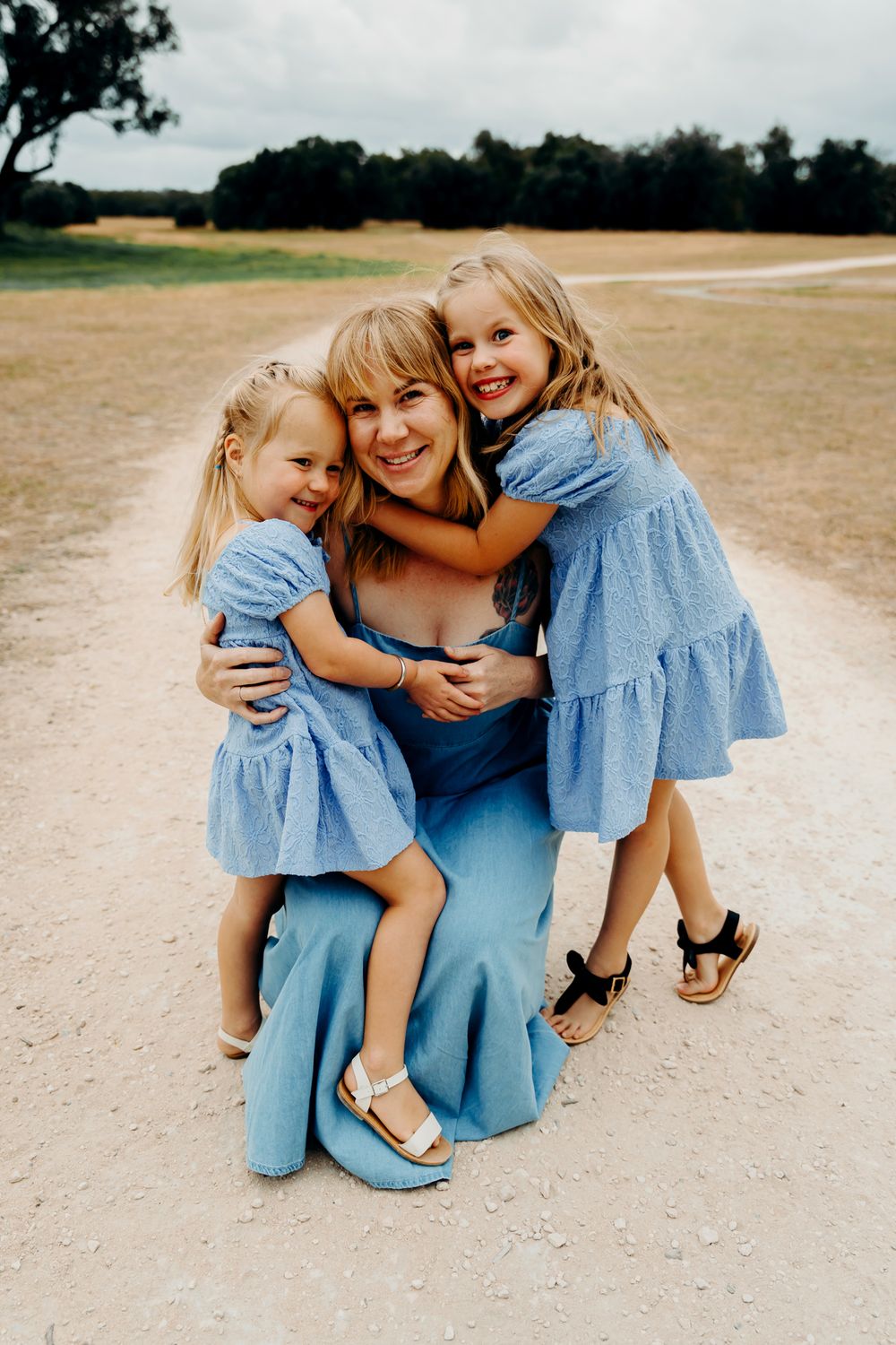 Candid moments of a family wearing coordinating blue outfits playing together on a sandy path during a sunny day.