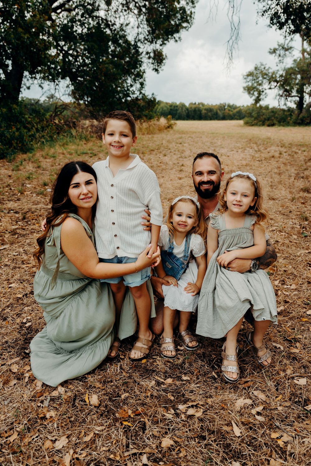 A family sits together on a hill covered in fallen leaves wearing coordinated sage green and gray outfits.