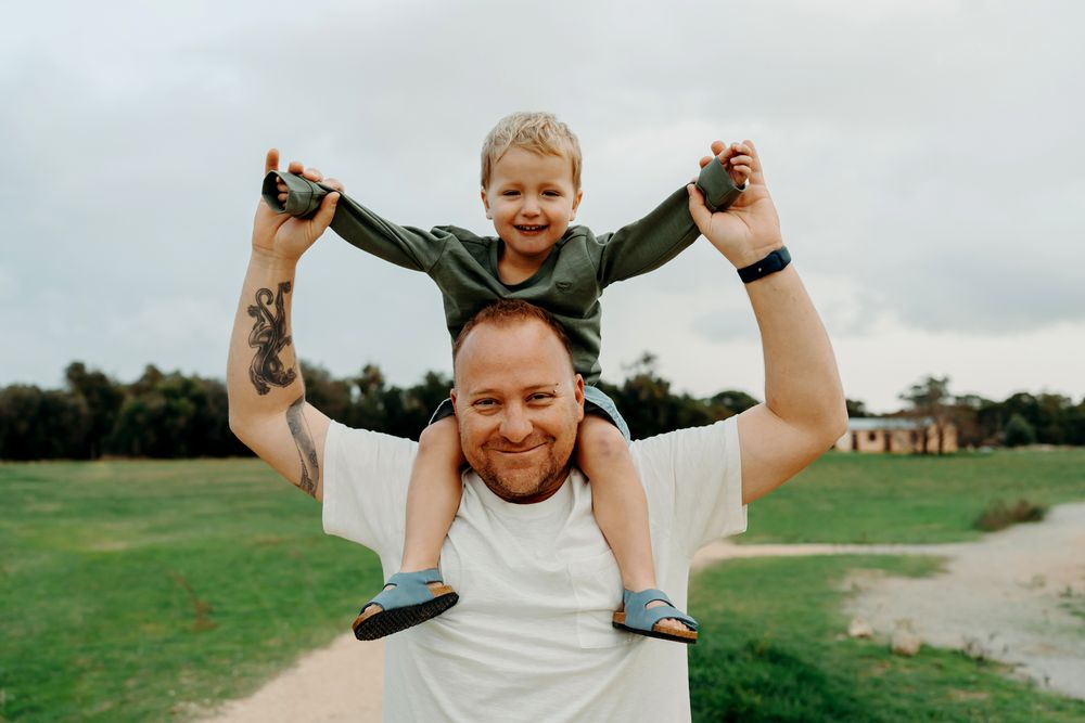 A joyful moment at a park with one person carrying another on shoulders against a cloudy sky background.