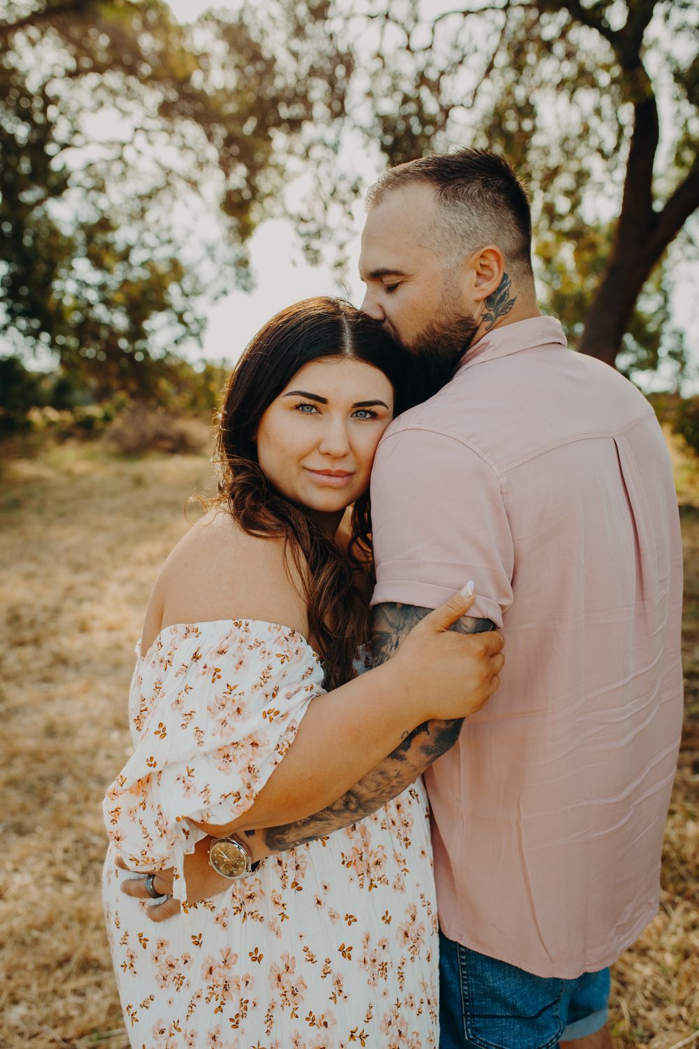 Two people embrace lovingly in a sun-dappled meadow on a warm summer evening.