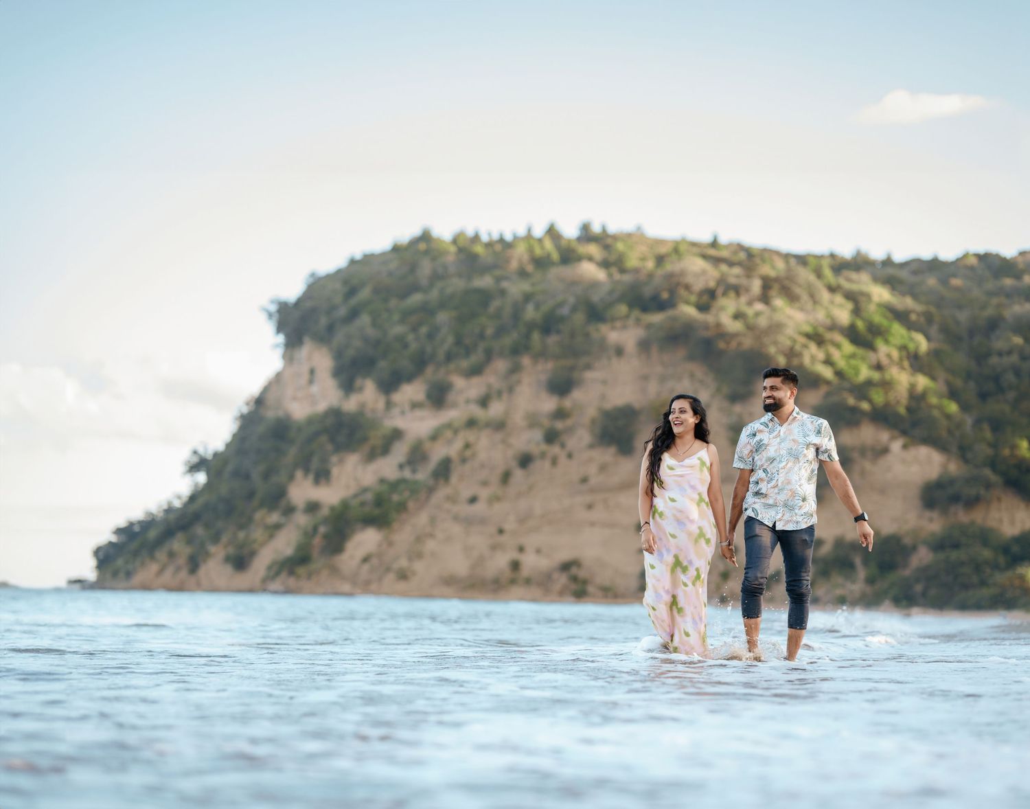 People stroll along a scenic beach with rocky cliffs and ocean waves at sunset creating a romantic beach scene.