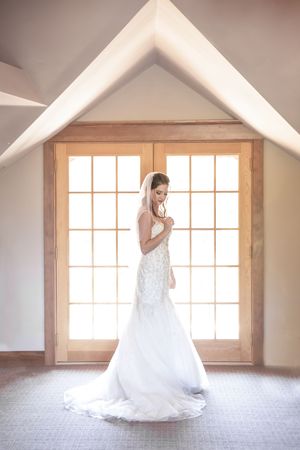 Silhouette of wedding dress against bright window in minimalist white room.