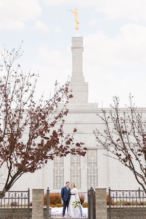 White temple building with ornate architecture framed by autumn trees and iron fence.