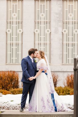 Wedding couple shares romantic moment outside ornate white building with architectural details.
