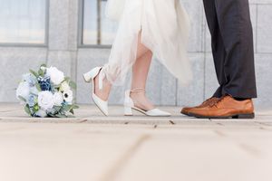 Close-up detail of wedding couple's feet and dress hem against light stone ground.