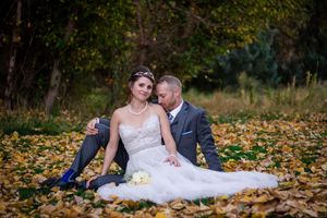 A romantic wedding photo with the couple sitting among fallen autumn leaves.