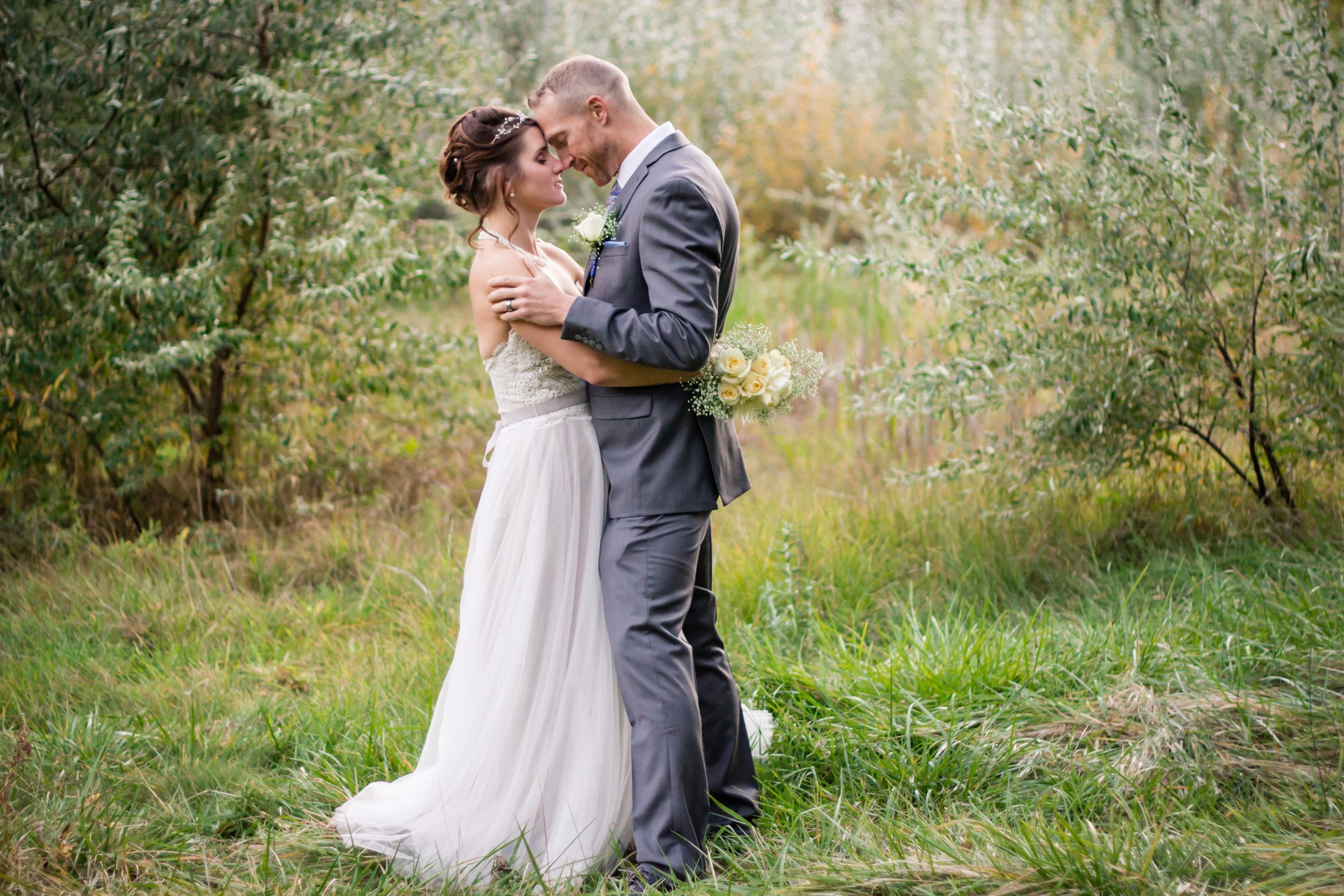 A tender moment between newlyweds in a natural outdoor setting with golden light.