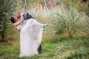 A joyful wedding couple embracing in a natural outdoor setting with tall grass.