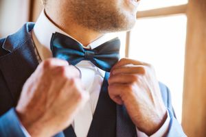 Close-up of adjusting blue bow tie against white formal shirt.