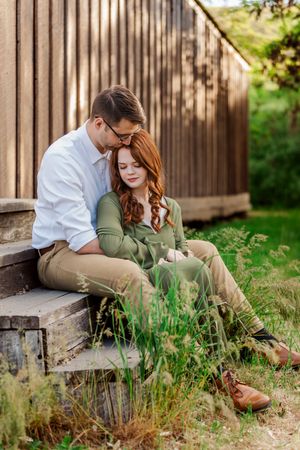 Intimate engagement photos taken on wooden deck surrounded by tall grass.