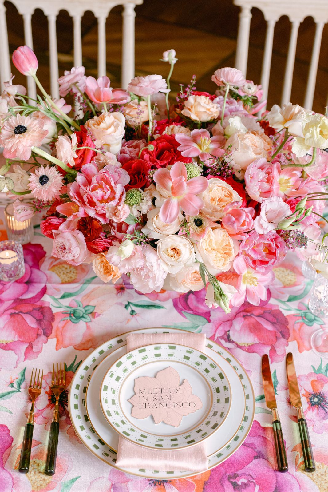 Elegant dining table set with pink and coral floral centerpieces and white place settings in a wood-paneled room.
