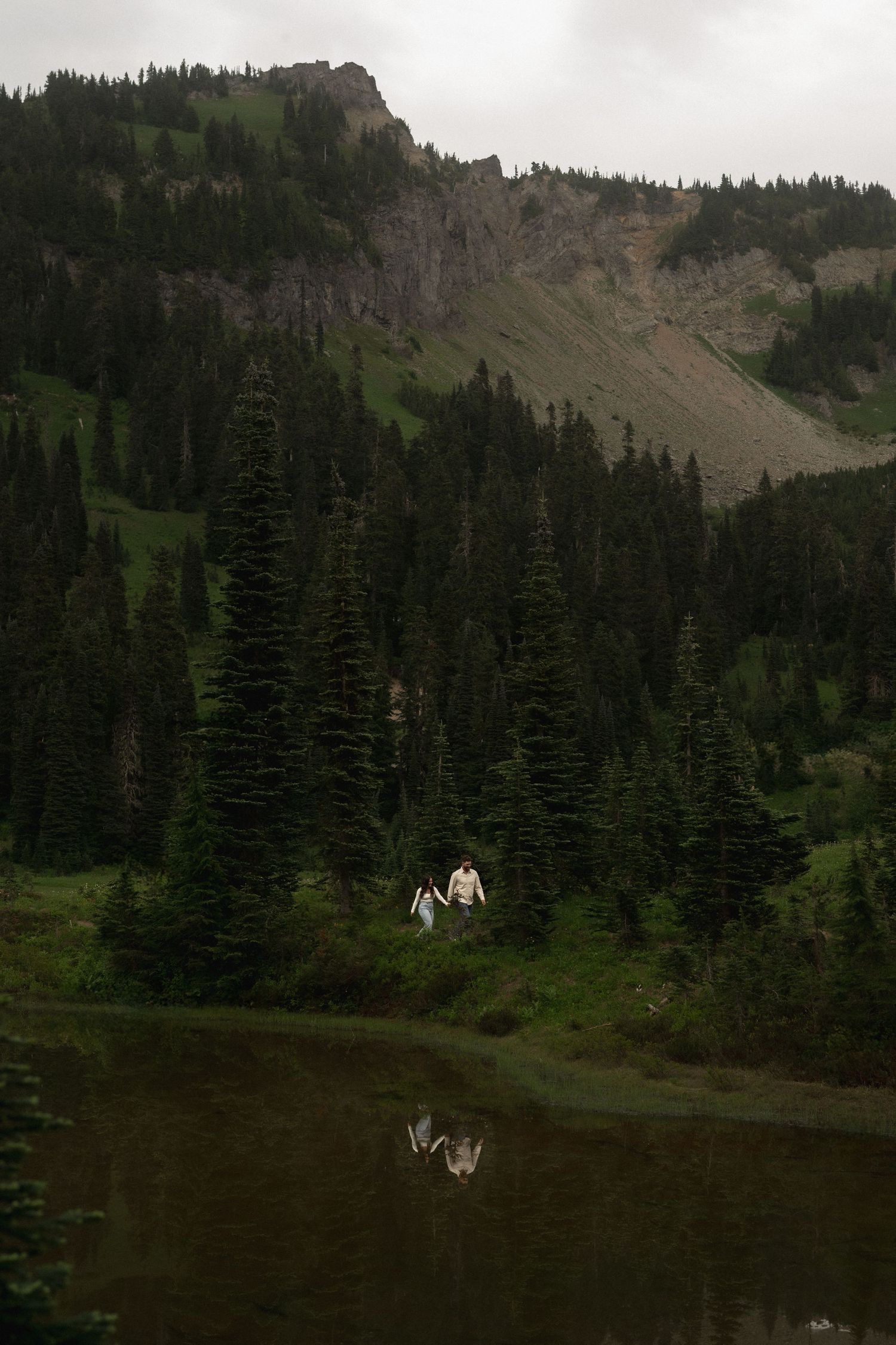 Two figures stand in a mountain meadow filled with white wildflowers at sunset.