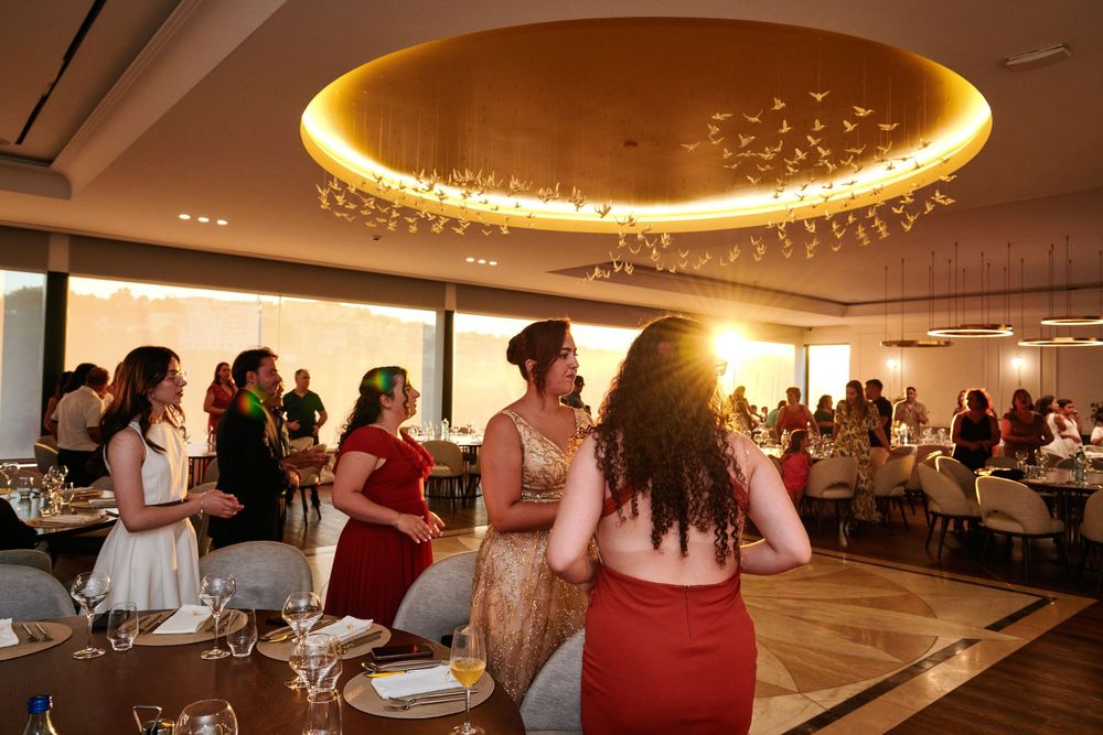Women in elegant dresses socializing and dancing inside a warmly lit modern event venue.