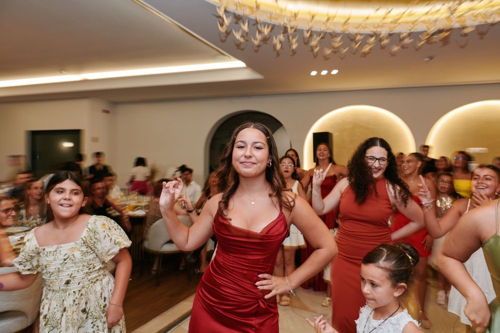 Woman in red dress dancing energetically with guests at a lively indoor celebration party.
