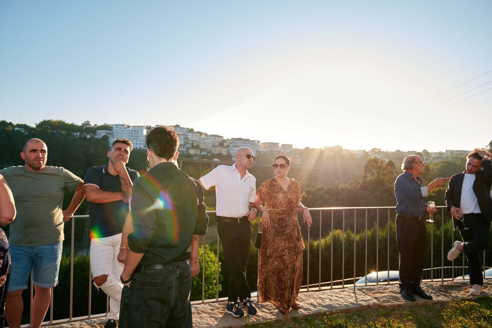 Group of guests socializing on a terrace overlooking lush greenery during a golden sunset event.