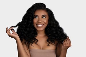Model showcases beautiful curly black hair while playfully touching her locks against a light background.