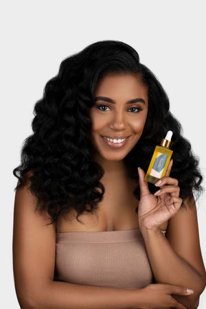 Model in beige top demonstrates hair oil product while showing off voluminous curls.