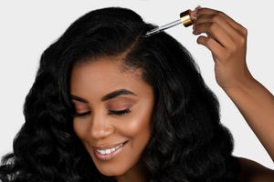 Close-up shot shows application of hair care product to dark curly hair.