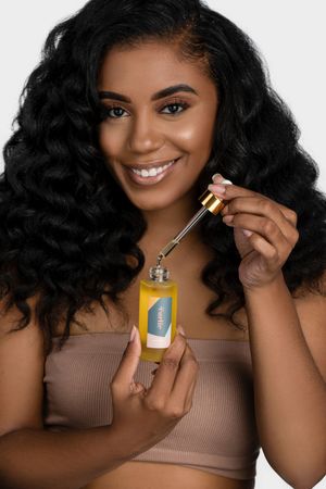 Model demonstrates hair oil product application while wearing neutral-toned crop top.