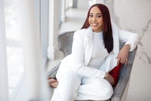 Woman in all-white business attire relaxing in modern grey armchair.