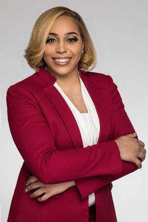 Executive in burgundy blazer and white top poses professionally against studio background.