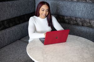 Woman in white sweater working on red laptop at marble table in grey booth.