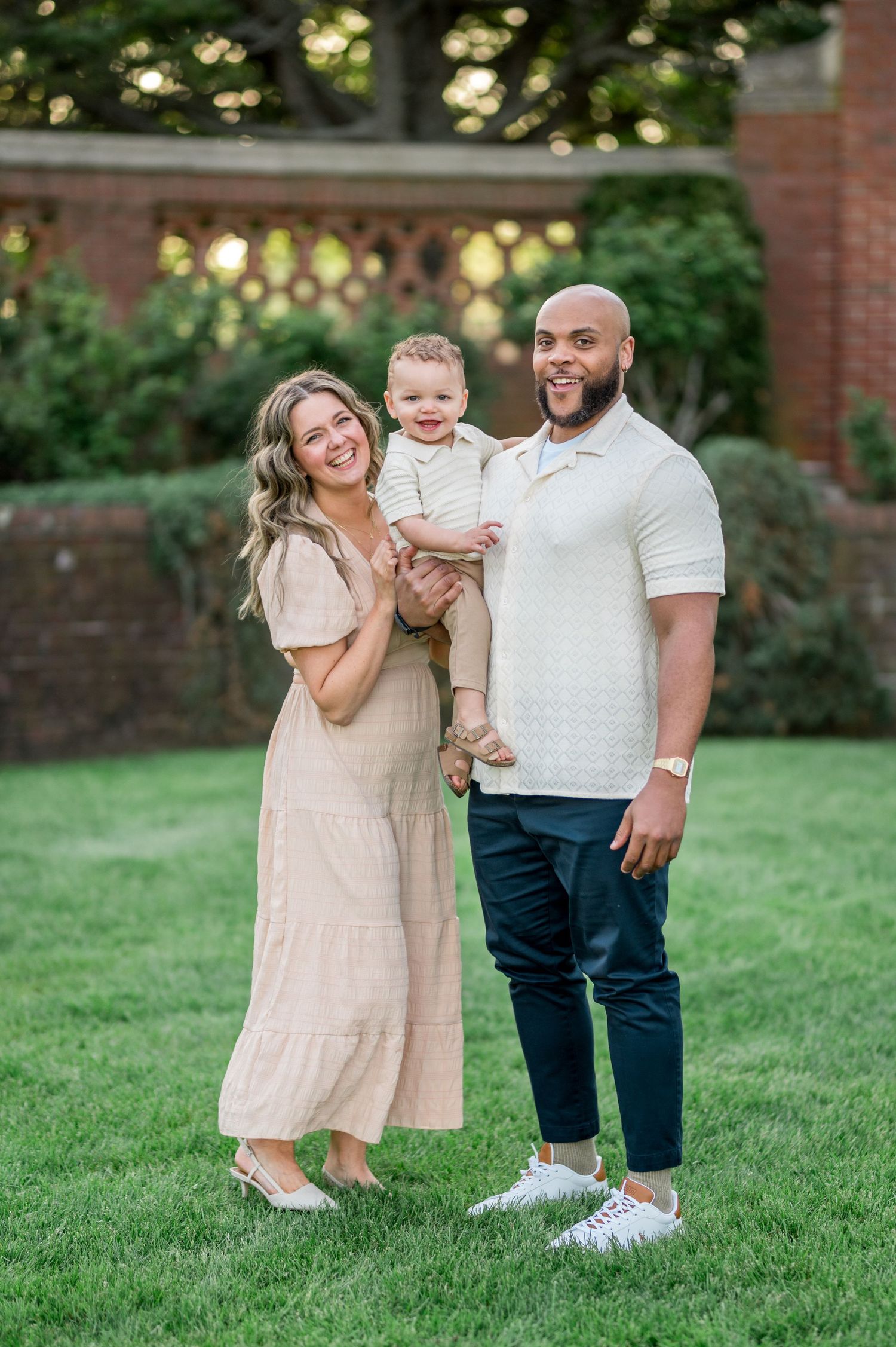 A family stands together on lush green grass while wearing coordinating cream and blue outfits on a sunny evening.