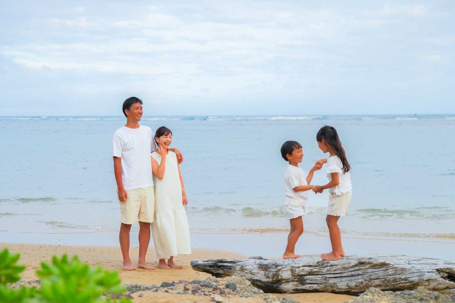 Fun family photo session with kids dancing at Kahala beach wearing white outfits having quality time at the beach on a tropical day.