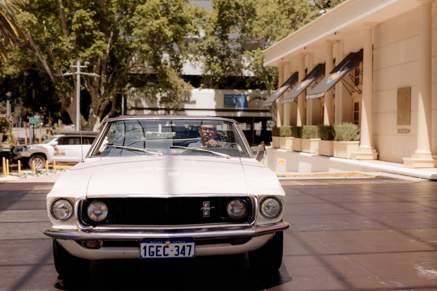 Vintage white Ford Mustang convertible with chrome grille photographed from front angle in an urban setting.