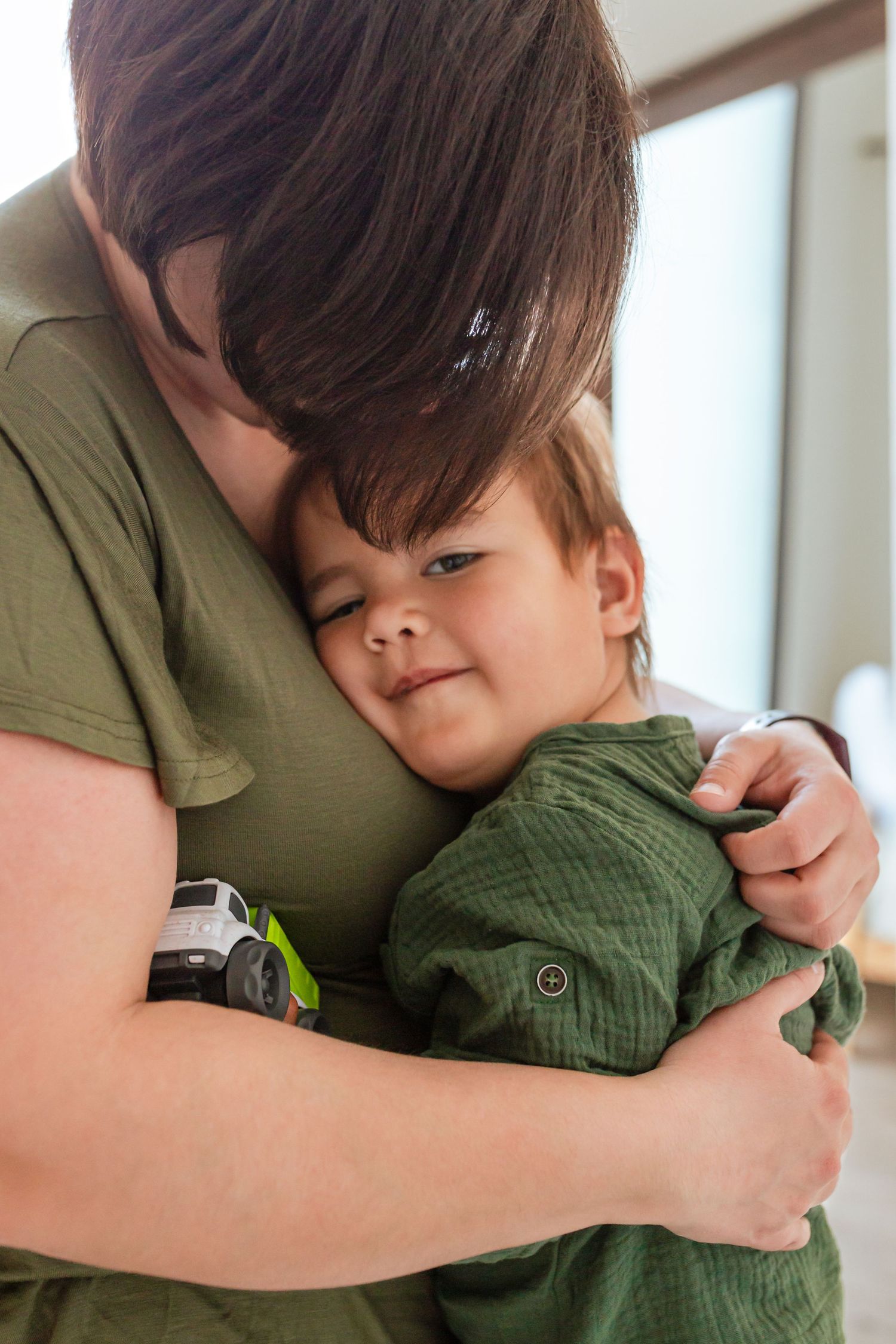 A tender moment captured as a parent in a green shirt hugs their young child who is also wearing green clothing.
