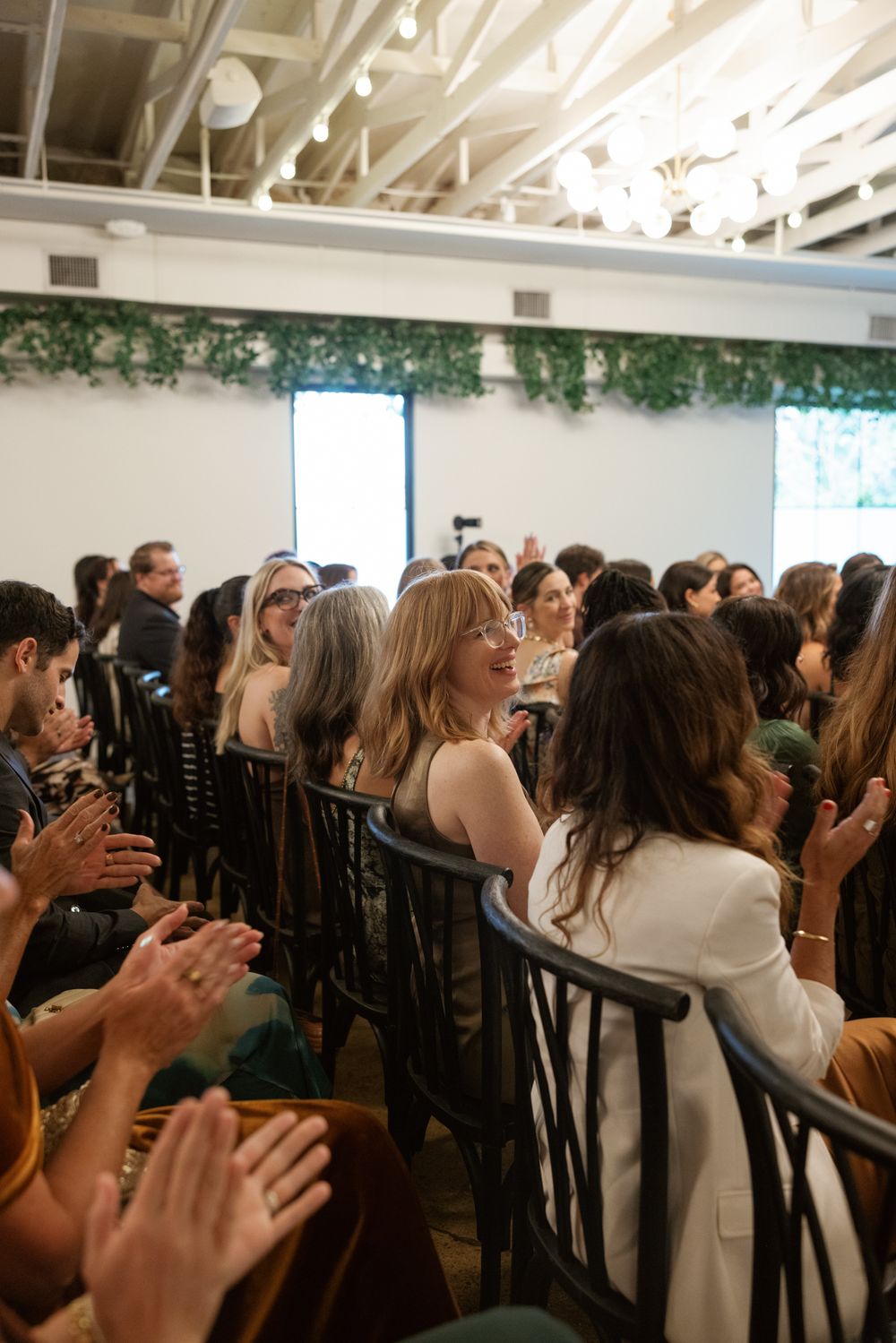 Audience members in a crowded venue clapping and showing enthusiasm during an indoor event.