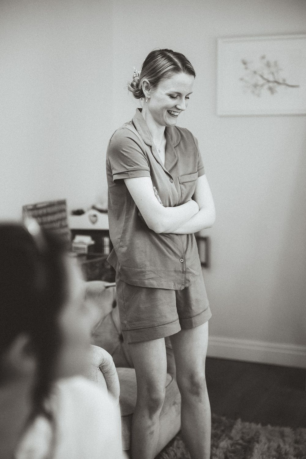 A black and white photo of someone wearing a casual short sleeve outfit standing against a wall with artwork.