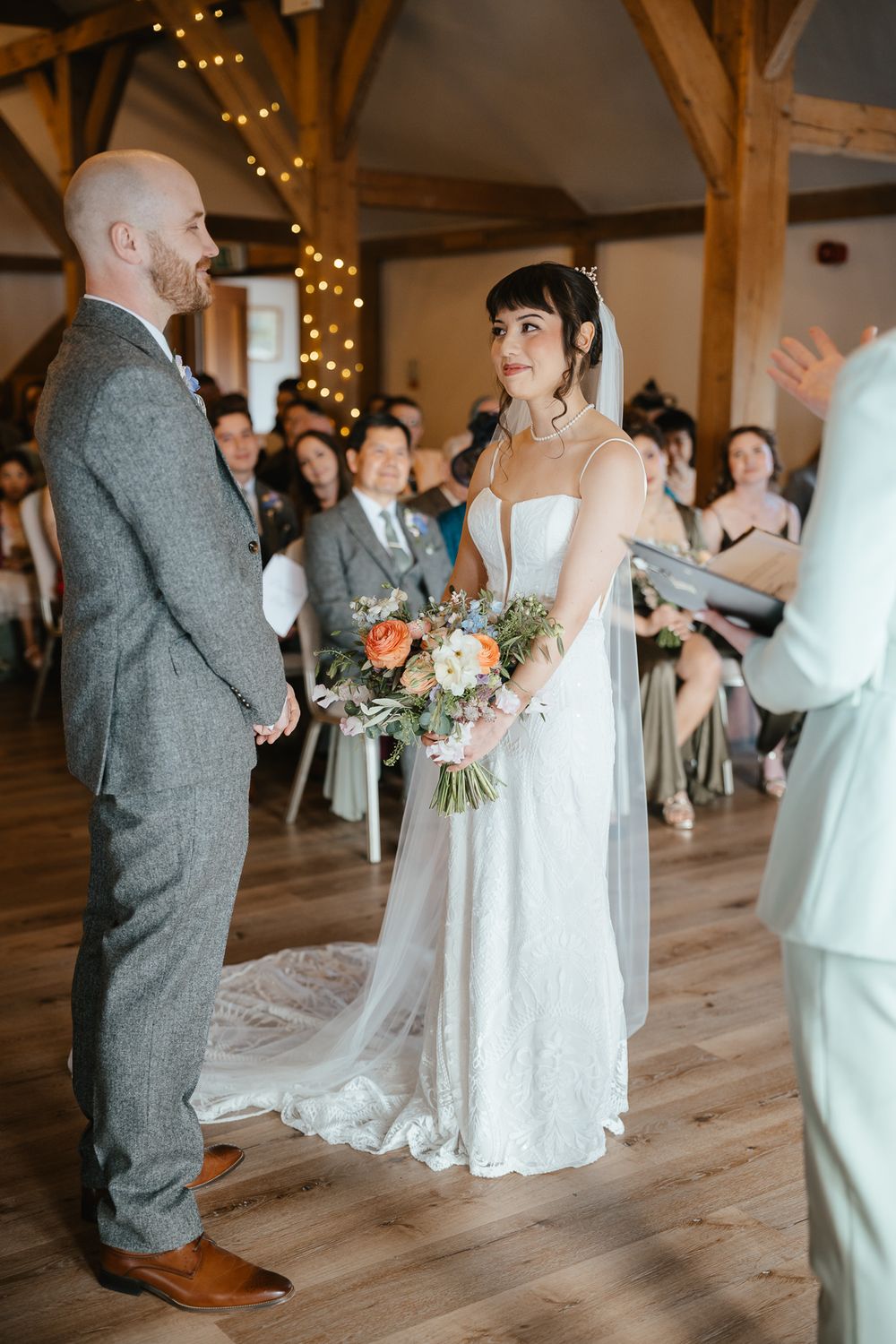 A romantic wedding ceremony in a rustic barn venue with twinkling lights and a couple exchanging vows on hardwood floors.