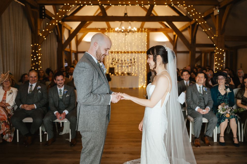 A rustic barn wedding ceremony with string lights and wooden beams overhead as a couple exchanges vows.