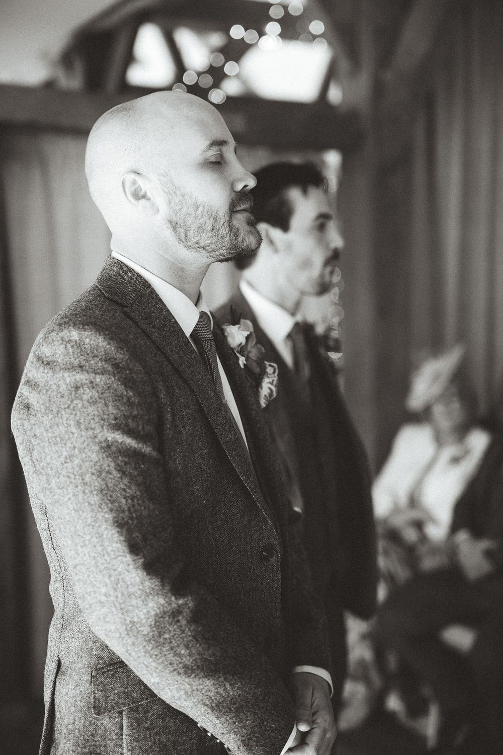 Four black and white photographs showing a person in a gray suit standing in an interior space viewed from different angles.